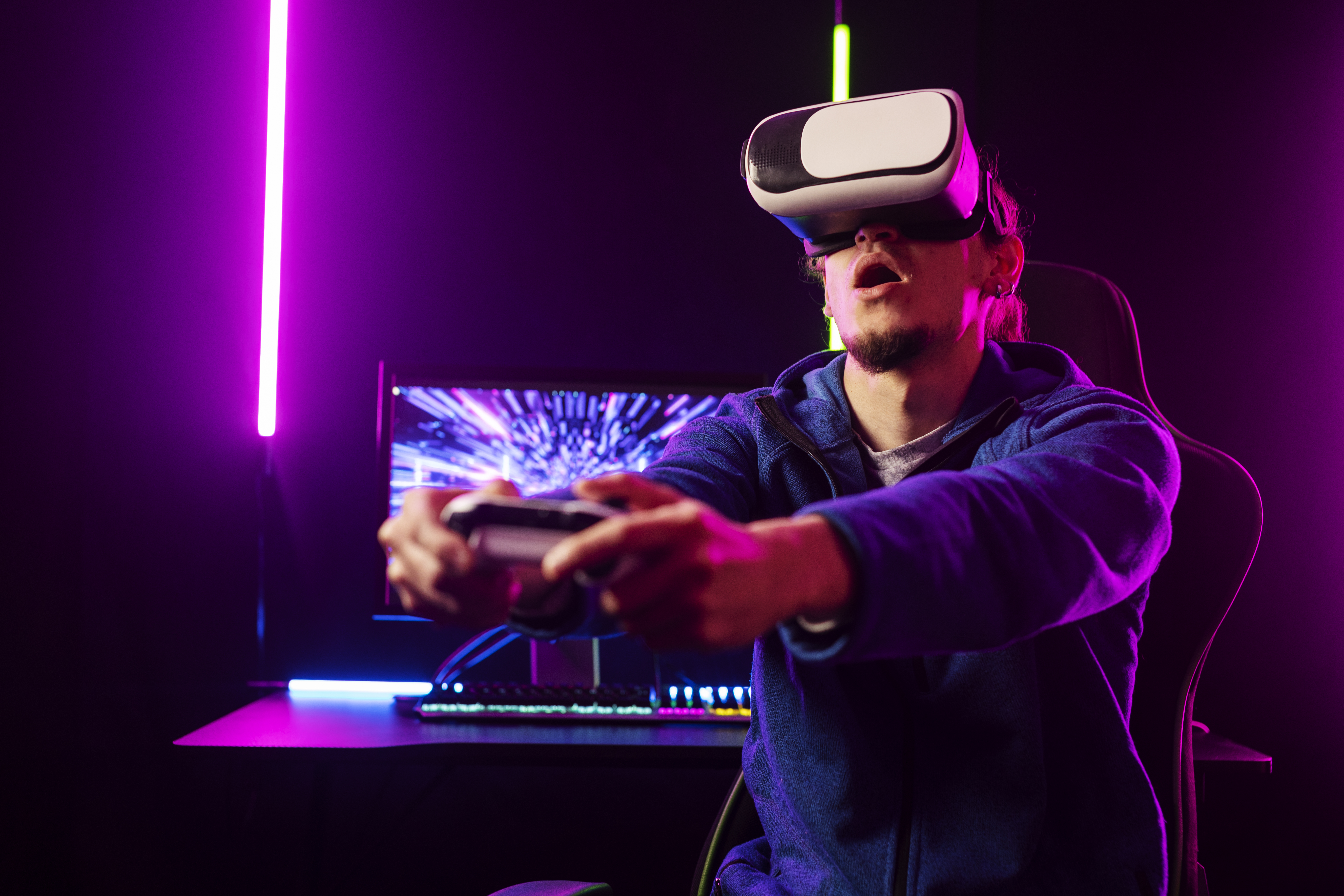 A gamer wearing a VR headset sits in front of a colorful, illuminated gaming setup
