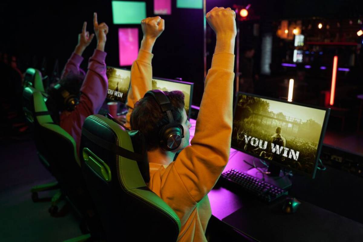 Two gamers celebrate victory with raised arms, wearing headsets, in a vibrant esports setting.