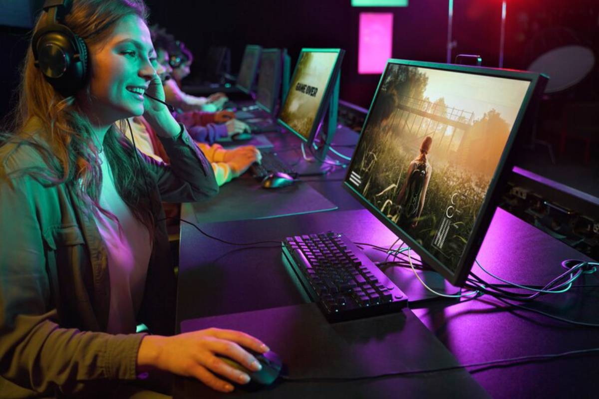 A gamer immersed in gameplay at a dimly lit computer station, with colorful lighting and multiple monitors displaying different games.