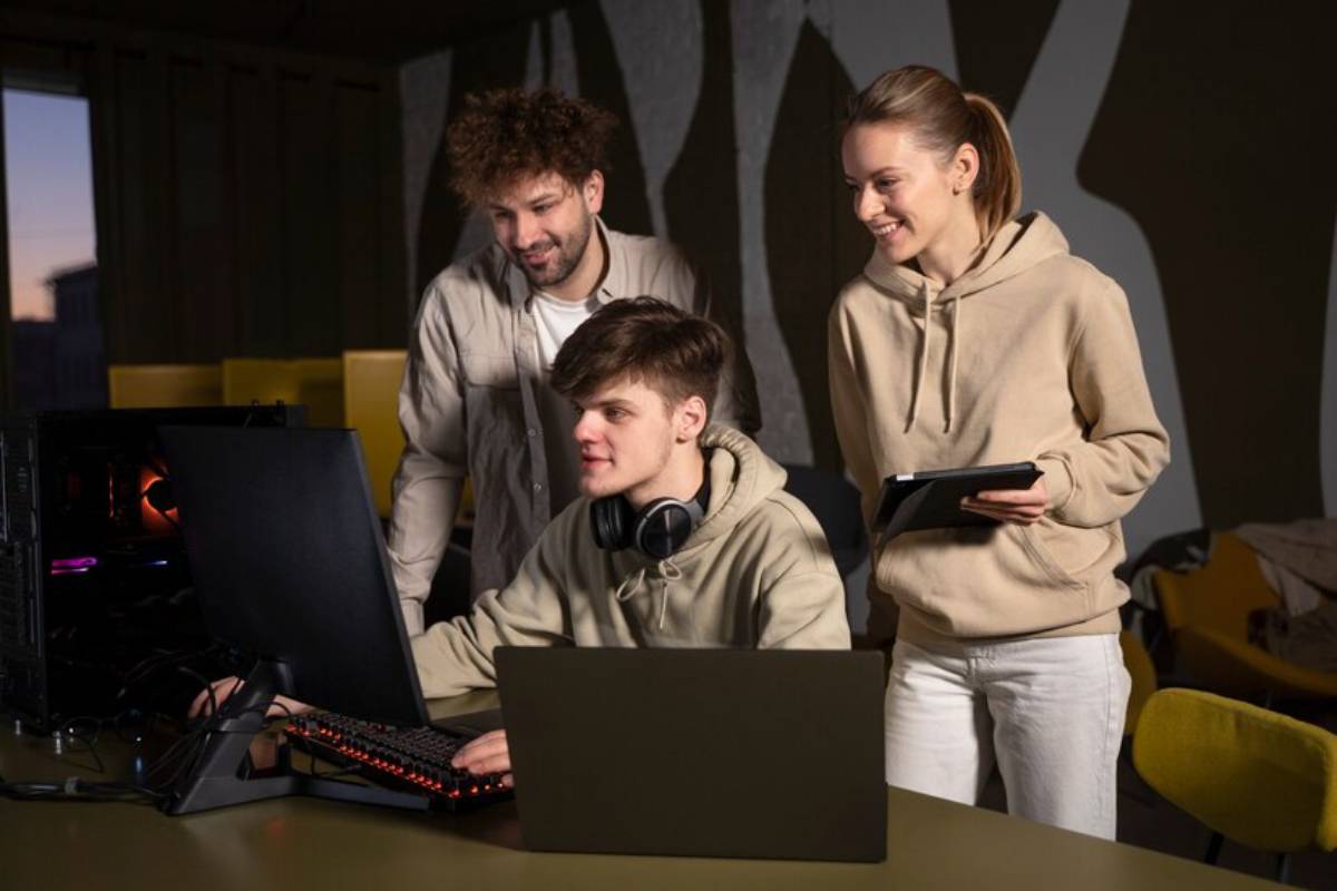 Three young people collaborate around a computer, playing game.
