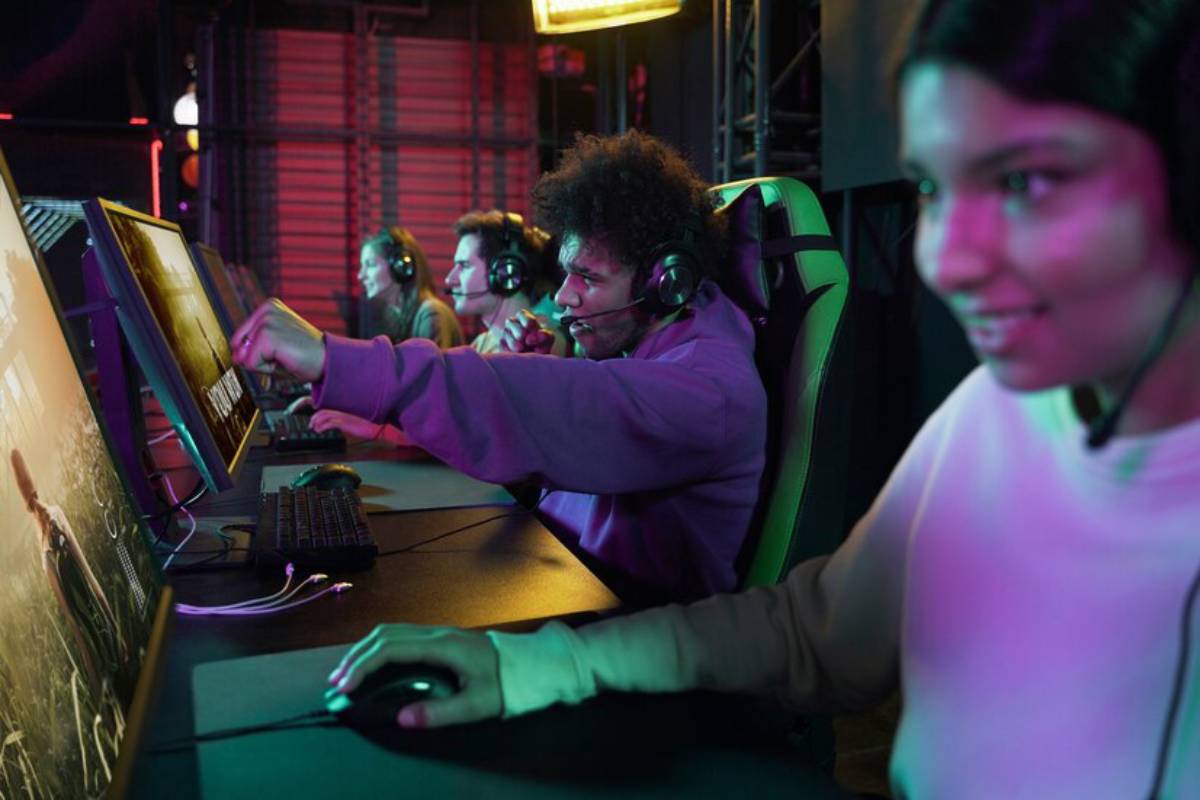 A group of gamers, wearing headsets, engaged in gameplay at high-tech gaming stations with colorful lighting around them.